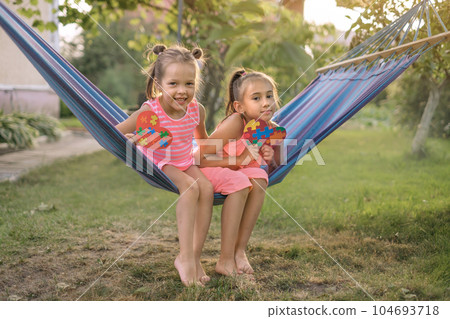 Charming hilarious sisters have fun in yard on hanging hammock Charming hilarious sisters have fun in yard on hanging hammock 104693718