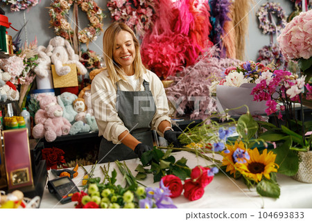 Smiling florist in the flower shop make bouquet for a holiday. Family flower's business 104693833
