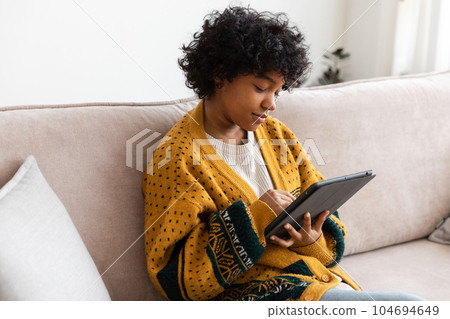 African american girl holding digital tablet touch screen typing scroll page at home. Woman with mobile tech device surfing internet using social media apps playing game. Study work shopping online 104694649