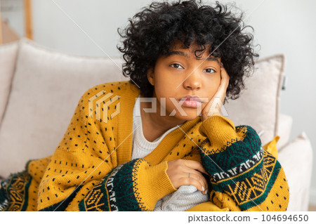 African american sad thoughtful pensive unmotivated girl sitting on sofa at home indoor. Young african woman ponder look tired after long day. Girl feels depressed offended lonely upset heartbreak 104694650