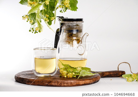 Teapot with brewed linden tea and a transparent glass on a white background. 104694668