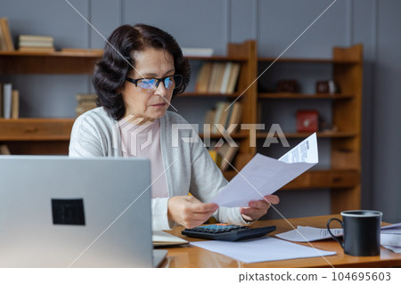 Middle aged senior woman sit with laptop and paper document. Pensive older mature lady reading paper bill pay online at home managing bank finances calculating taxes planning loan debt pension payment Middle aged senior woman sit with laptop and paper document. Pensive older mature lady reading paper bill pay online at home managing bank finances calculating taxes planning loan debt pension payment 104695603