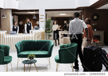 African american couple at reception, arriving at hotel and preparing to do check in process. Happy man and woman asking front desk staff about room reservation, fill in registration forms. African american couple at reception, arriving at hotel and preparing to do check in process. Happy man and woman asking front desk staff about room reservation, fill in registration forms. 104695693
