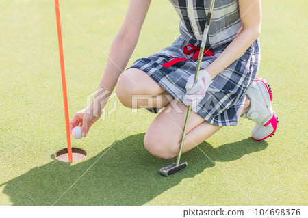 Golfer woman taking golf ball out of cup on golf course 104698376