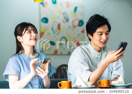 A couple who concentrates on a smartphone during a date A couple who concentrates on a smartphone during a date 104698528