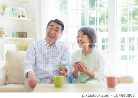 一對老夫婦在客廳裡看智能手機 104698802