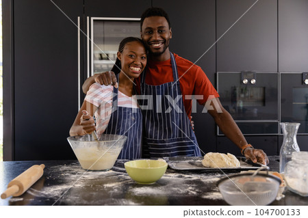 Portrait of happy african american couple in aprons preparing bread dough in kitchen Portrait of happy african american couple in aprons preparing bread dough in kitchen 104700133