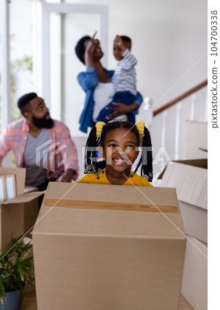Smiling african american daughter and father carrying boxes with family in background at new home Smiling african american daughter and father carrying boxes with family in background at new home 104700338