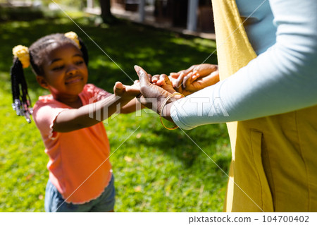 Midsection of african american mother holding daughter's hands in backyard on sunny day 104700402