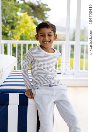 Portrait of happy biracial boy wearing pyjamas in bedroom in front of window with view of treetops Portrait of happy biracial boy wearing pyjamas in bedroom in front of window with view of treetops 104700416