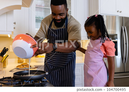 Happy african american father with daughter cooking pancakes in pan in kitchen 104700495