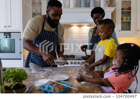 African american children playing with flour while parents making pancakes in kitchen 104700497