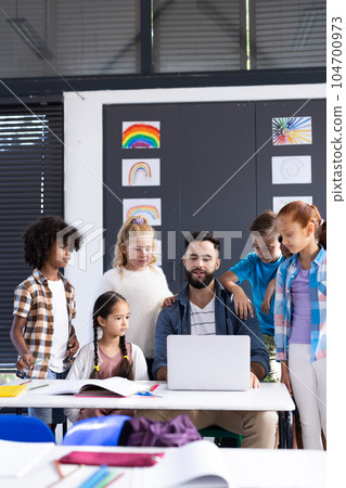 Vertical of diverse elementary schoolchildren and male teacher using laptop in classroom, copy space Vertical of diverse elementary schoolchildren and male teacher using laptop in classroom, copy space 104700973