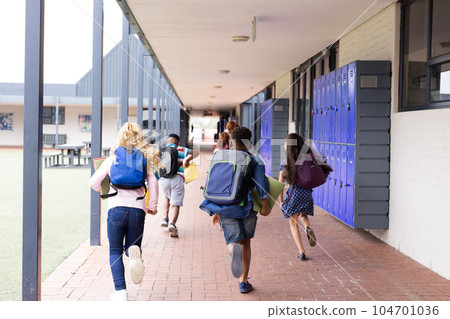 Rear view of diverse children with schoolbags running in elementary school corridor, copy space Rear view of diverse children with schoolbags running in elementary school corridor, copy space 104701036