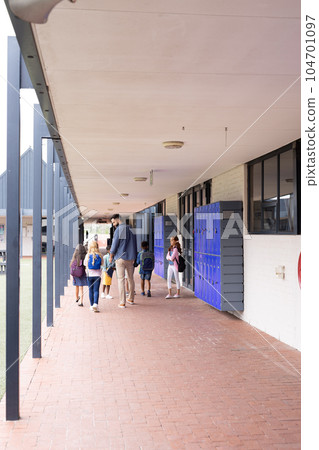 Vertical rear view of diverse male teacher and children in elementary school corridor, copy space Vertical rear view of diverse male teacher and children in elementary school corridor, copy space 104701097