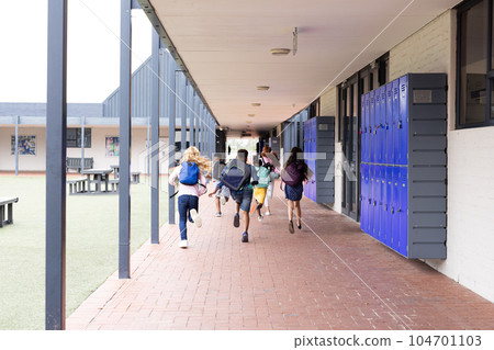 Rear view of diverse children with schoolbags running in elementary school corridor, copy space Rear view of diverse children with schoolbags running in elementary school corridor, copy space 104701103