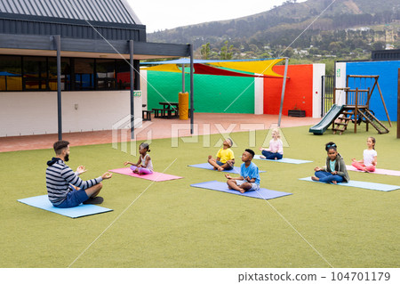 Diverse male teacher and elementary schoolchildren practicing meditation in schoolyard Diverse male teacher and elementary schoolchildren practicing meditation in schoolyard 104701179