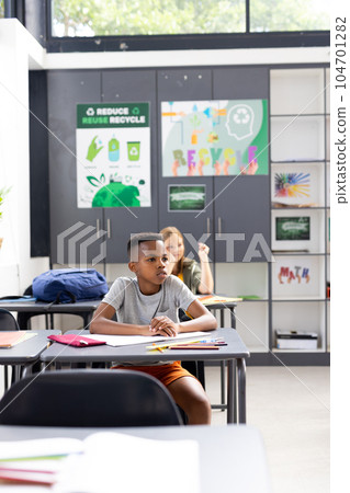 Vertical of african american schoolboy sitting at desk listening in classroom, copy space Vertical of african american schoolboy sitting at desk listening in classroom, copy space 104701282