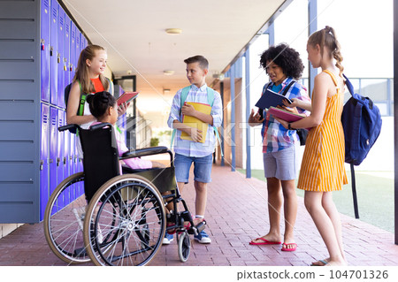 Happy diverse school children talking with girl in wheelchair in school corridor copy space 104701326