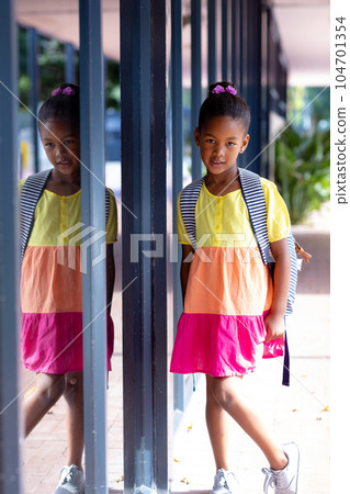 Biracial schoolgirl with school bag leaning on wall in school corridor, with copy space 104701354