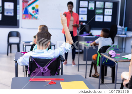 Diverse female teacher and boy with raised hand in class Diverse female teacher and boy with raised hand in class 104701356