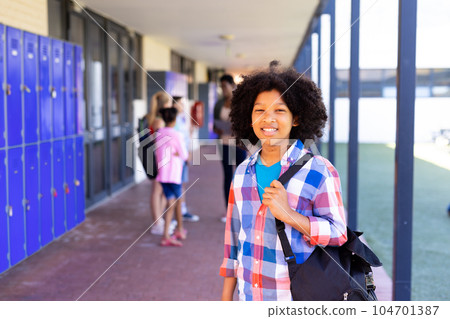 Portrait of smiling biracial schoolgirl standing with bag in school corridor with copy space Portrait of smiling biracial schoolgirl standing with bag in school corridor with copy space 104701387