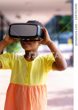 Biracial schoolgirl using vr headset in sunny school corridor, with copy space 104701440
