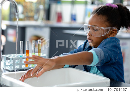Biracial schoolgirl in safety glasses washing hands in science class Biracial schoolgirl in safety glasses washing hands in science class 104701467