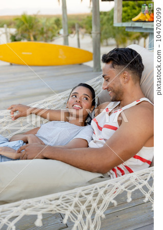Smiling biracial young couple looking at each other while relaxing on hammock at beach 104702099