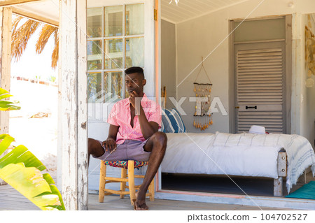 Thoughtful biracial man looking away sitting on porch at summer beach house, copy space 104702527