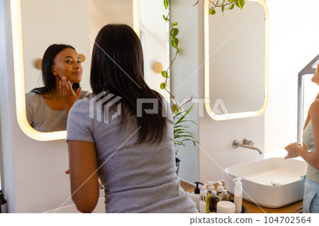 Happy biracial lesbian couple looking in mirrors in bathroom 104702564