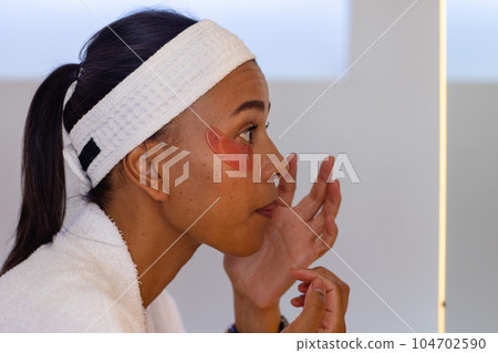 Biracial woman in bathrobe wearing eye mask in bathroom 104702590