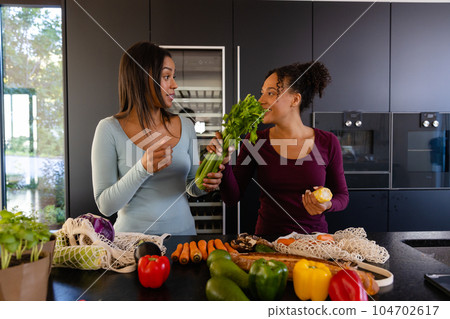 Happy biracial lesbian couple unpacking groceries in kitchen 104702617