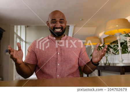 Happy biracial woman sitting at table having video call at home, gesturing and smiling 104702679
