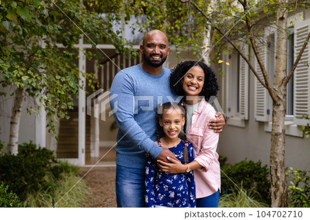 Portrait of happy biracial parents and daughter embracing in garden outside house 104702710