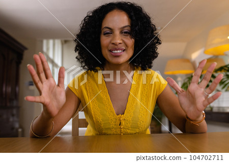 Happy biracial woman sitting at table having video call at home, gesturing and smiling 104702711