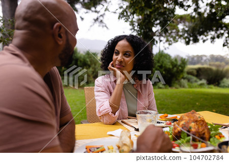 Happy biracial couple having meal and talking sitting at table in garden 104702784