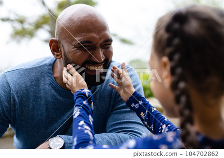 Smiling biracial father with daughter touching beard in garden 104702862