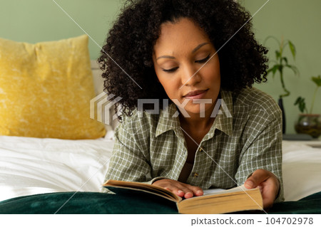 Biracial woman reading book lying on bed in bedroom Biracial woman reading book lying on bed in bedroom 104702978
