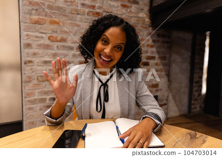 Happy biracial casual businesswoman making video call and waving in office 104703014