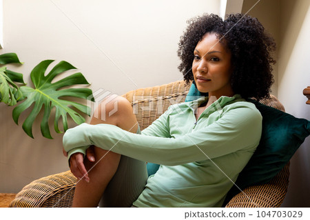 Happy biracial woman sitting on woven armchair at home Happy biracial woman sitting on woven armchair at home 104703029
