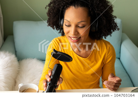 Happy biracial woman using headphones and microphone podcasting from home 104703164