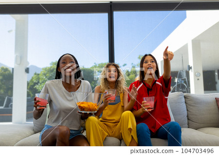 Group of excited diverse friends sitting on sofa, watching sport on tv and pointing Group of excited diverse friends sitting on sofa, watching sport on tv and pointing 104703496