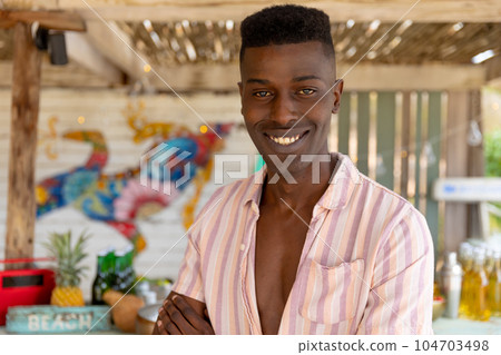 Portrait of happy biracial man standing in sunny beach bar smiling, unaltered 104703498