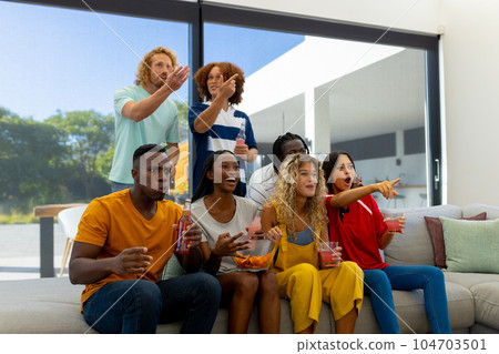 Group of focused diverse friends sitting on sofa, watching sport of tv Group of focused diverse friends sitting on sofa, watching sport of tv 104703501