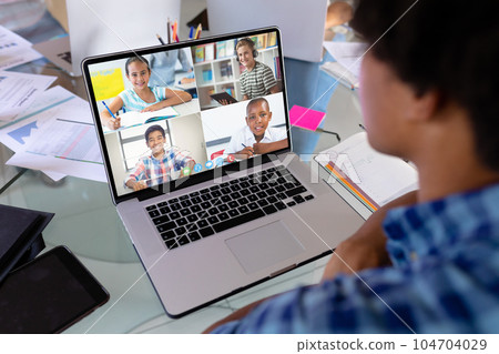 Diverse students at table with documents having laptop video call 104704029
