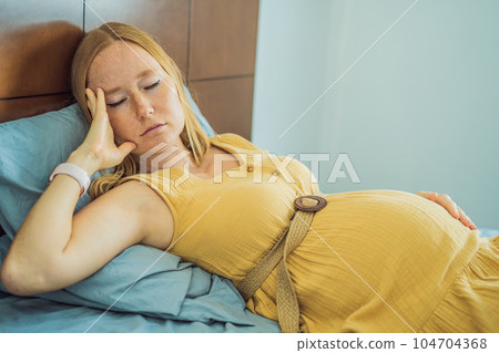 A stressed tired pregnant mother lying in bed at home. Morning sickness and nausea A stressed tired pregnant mother lying in bed at home. Morning sickness and nausea 104704368
