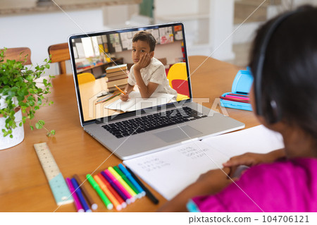 Multiracial girl discussing homework with boy over laptop while studying online on table at home 104706121
