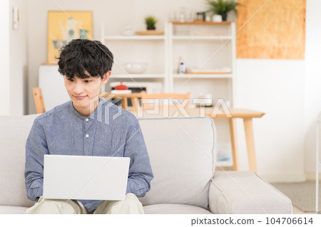 Young man sitting on a sofa and using a laptop on his lap 104706614