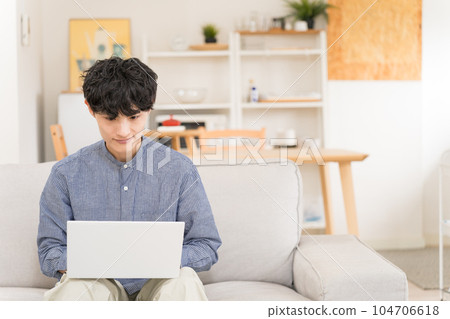 Young man sitting on a sofa and using a laptop on his lap 104706618